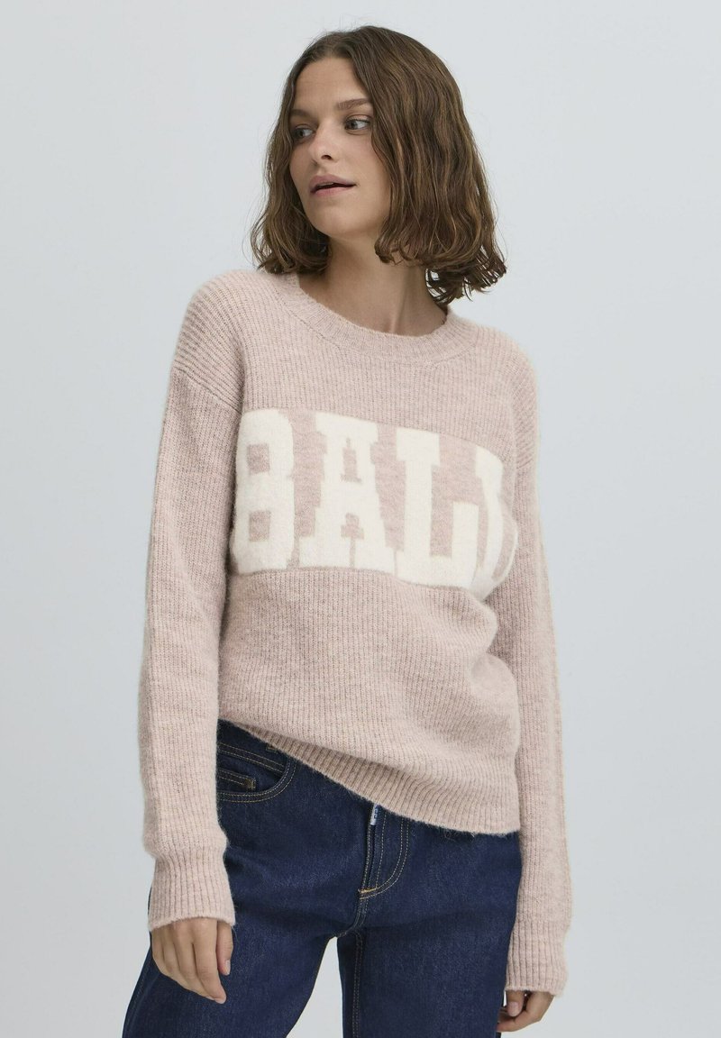 Šviesiai rožinė megzta džemperis su ilgomis rankovėmis ir raštuotu paviršiumi, su ryškiu baltu "BALI" logotipu per krūtinę.