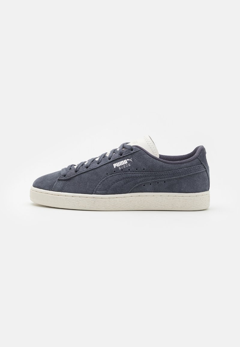 Baskets en daim bleu marine avec des accents blancs et une semelle en caoutchouc texturée. Présentent des perforations sur le côté et des lacets plats. Design classique à coupe basse.