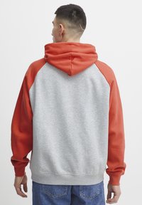 Sudadera con capucha de mangas rojas y cuerpo gris. Cuenta con un bolsillo canguro y puños acanalados. Textura suave, ajuste casual.