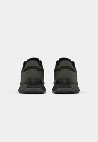Paire de baskets noires et gris foncé vues de dos sur un fond uni gris clair.