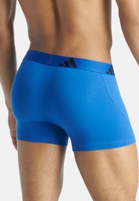 Modré pružné bavlněné boxerky s širokým modrým pasem a černými akcenty loga Adidas. Hladký povrch, přiléhavý střih.