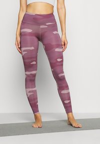 Legginsy o wysokim stanie w fioletowym wzorze maskującym. Wykonane z elastycznego materiału o gładkiej fakturze i elastycznej talii.