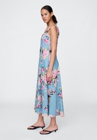 Blomstret midikjole i lyseblått stoff, med rund hals, ermeløs design og store rosa og lilla blomstermønstre.