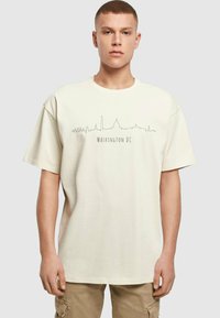 Tricou din bumbac bej, cu o croială relaxată, av�ând un contur grafic al orizontului orașului Washington DC și textul „WASHINGTON DC” dedesubt.