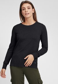 Maglione nero a maniche lunghe con scollatura rotonda e polsini a costine, con dettaglio di spacco laterale e una piccola accentatura con logo vicino all'orlo.