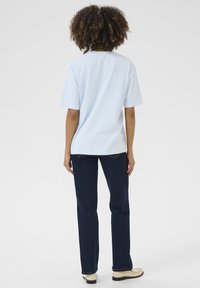 T-shirt en coton bleu clair à coupe décontractée, avec des manches courtes et un col rond, associé à un jean droit bleu foncé et des chaussures beiges.