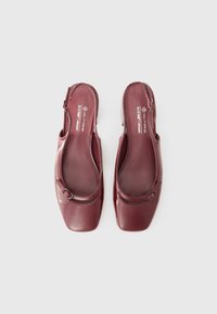 Talons slingback en cuir vegan bordeaux avec un design à bout carré, mettant en avant un détail de boucle arrondi sur la sangle avant et une texture lisse.