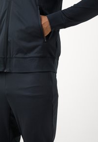 Navi sportlik jakk sileda tekstuuriga, varustatud lukustatava tasku ja soonikutessega mansettidega, koos sobivate pükstega.