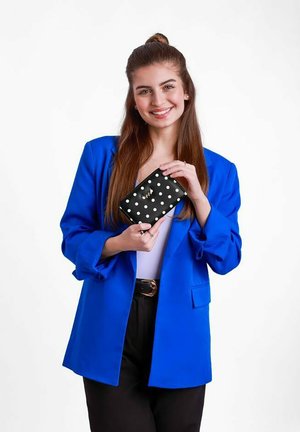 Černá peněženka s puntíky držená v rukou, s hladkým povrchem a zlatými akcenty, na pozadí jasně modrého saku.