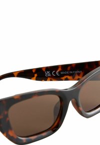 Lunettes de soleil en écaille de tortue avec des verres rectangulaires. Verres dégradés marron, monture en plastique lisse, étiquettes 'CE' et 'UKCA' sur la branche.