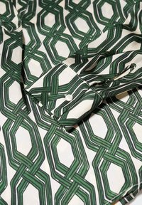 Gros plan sur une chemise en tissu blanc avec un motif géométrique en chaîne verte et un poignet boutonné.
