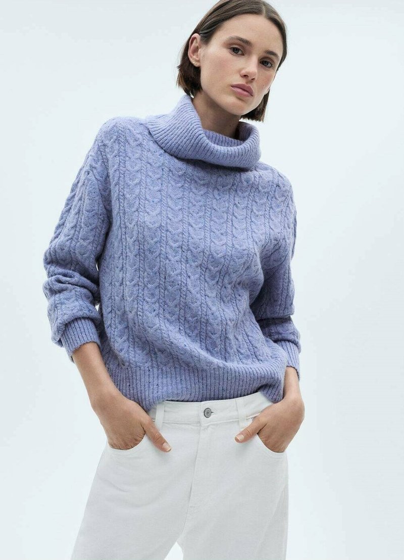 Maglione viola lavorato a maglia con un colletto alto e ripiegato, motivo a treccia testurizzato e polsini a costine; indossato con pantaloni bianchi.