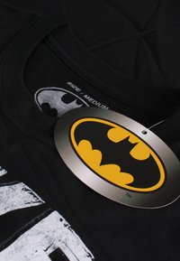 Black cotton T-shirt featuring a gray Batman graphic and a yellow and black hangtag with the Batman logo, labeled size medium.