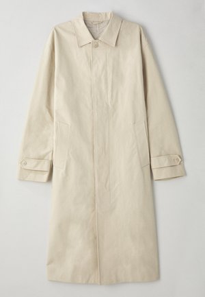 Beige, knälång kappa tillverkad av bomullsblandat tyg. Har en revärkrage, knappstängning fram och sidofickor med lockdetalj.