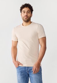 Beige, rövid ujjú póló kerek nyakkivágással, puha pamutból készült, kék farmernadrággal párosítva, amely slim-fit kialakítással rendelkezik.