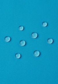 Gocce d'acqua trasparenti su una superficie blu texturizzata, di varie dimensioni e disposte casualmente, che mostrano una finitura lucida e una forma circolare ben definita.