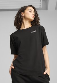 Camiseta de algodón negra con un corte holgado, mangas cortas y un logo blanco de Puma en el pecho. Textura suave, diseño básico.