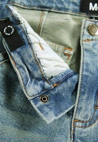 Vaqueros de denim de color azul desgastado, con costuras naranjas en contraste y cierre de botón a presión. Presentan una etiqueta negra y un diseño de bolsillo reforzado.