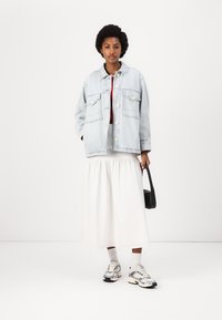 Ljusblå denimjacka med stora fickor, vit flödande kjol, röd topp och silverfärgade sneakers; accessoriserad med en liten svart handväska.