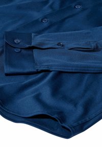 Tmavomodrá košeľa na gombíky s dlhými rukávmi, s prehnutým manžetovým lemom a viditeľnými štyrmi gombíkmi, s hladkou textúrou látky.