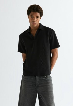 Schwarzes Polohemd mit kurzen Ärmeln und strukturiertem Muster sowie kontrastierendem Kragen. Kombiniert mit dunklen Denim-Jeans.