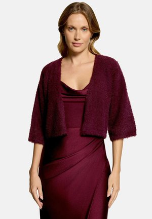 Kvinde iført en ærmeløs bordeaux kjole med draperet halsudskæring og en matchende cropped, blød cardigan med trekvartærmer.