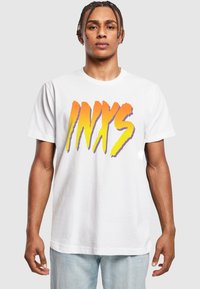 Hvid bomulds t-shirt med et iøjnefaldende tryk af "INXS" i orange og lilla. Kortærmet med rund halsudskæring. Løs pasform.