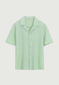 Chemise à manches courtes de couleur vert clair, en tissu texturé. Présente un col en V et cinq boutons assortis sur le devant.