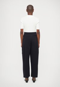 Witte geribbelde top met korte mouwen gecombineerd met zwarte broek met wijde pijpen, met een relaxte pasvorm en een elastische tailleband. Glad, zacht textuur.