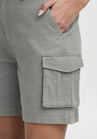 Shorts cargo gris en tissu résistant avec poches latérales, une poche à rabat sur la cuisse et des détails de surpiqûres contrastants.