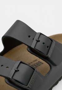 Sandalo Birkenstock nero con due cinturini regolabili con fibbie quadrate, plantare in sughero sagomato e suola in gomma testurizzata.