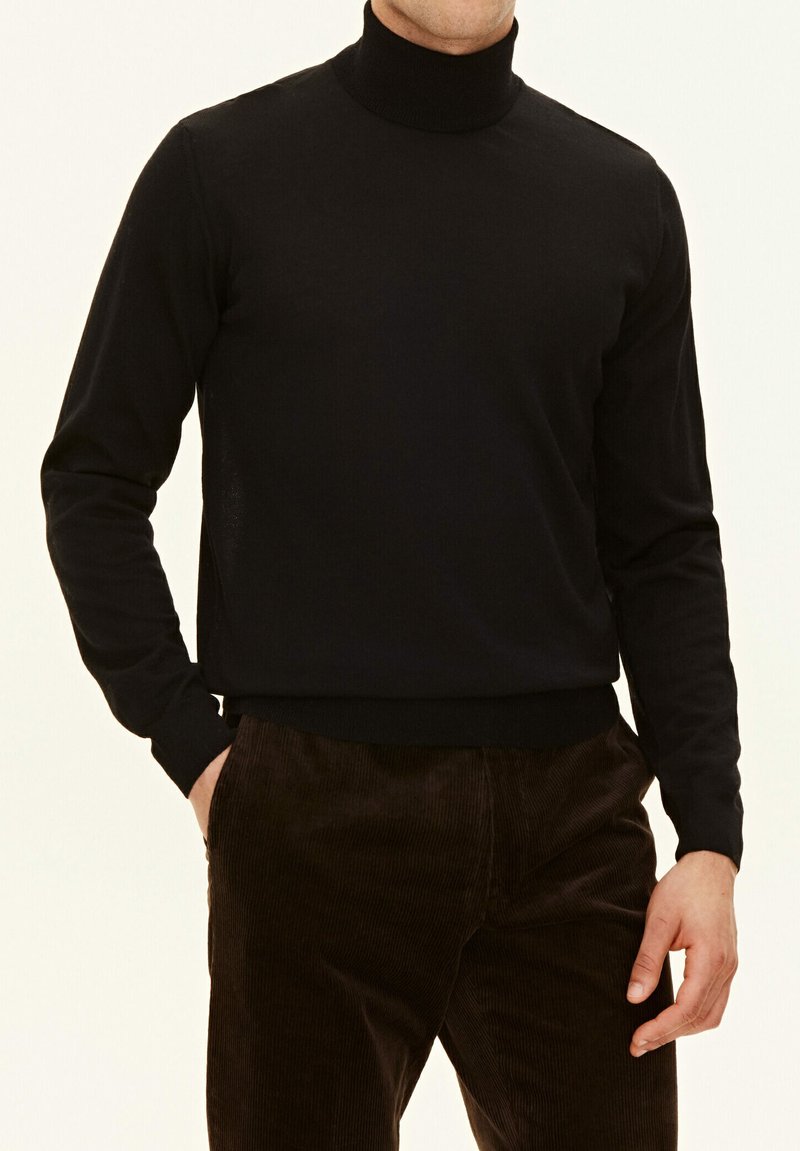 Maglione a collo alto di colore nero realizzato in un tessuto liscio, con maniche lunghe e orlo aderente, abbinato a pantaloni in corduroy marrone.