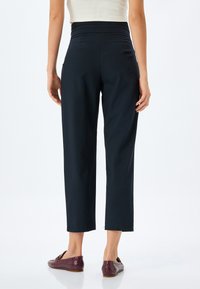 Zwarte, hoog-waist broeken met een rechte pijp. Materiaal lijkt glad; heeft een nette zoom en twee zijzakken. Gepaard met bordeauxrode instappers.