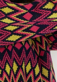 Sweter dziergany z wyraźnym geometrycznym wzorem w kolorach różowym, żółtym i granatowym. Wzór zawiera kształty rombów oraz motywy zygzakowate.