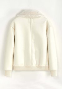 Veste couleur crème avec un col doux et moelleux, des poignets et un ourlet côtelés. Présente un matériau extérieur lisse et texturé ainsi qu'un design minimaliste.