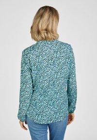 Langarmhemd mit einem abstrakten Muster in Blau, Grün und Weiß. Weicher Stoff, runder Halsauschnitt und detaillierte Knopfmanschetten.