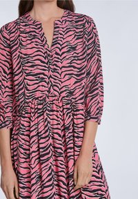 Robe rose et noire à rayures zébrées, avec un décolleté en V, des manches trois-quarts et une taille froncée, associée à une jupe fluide.