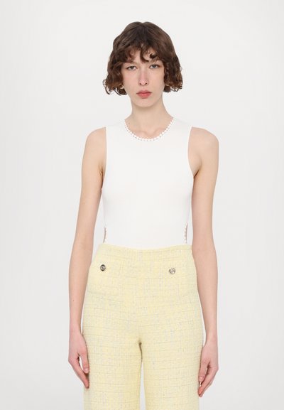Bodysuit blanc sans manches avec un relief texturé et un col festonné, associé à un pantalon taillé jaune clair avec deux boutons à l'avant.