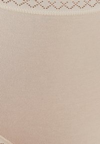Culotte haute nude sans couture avec une dentelle texturée au niveau de la taille. Tissu doux et lisse avec un léger motif à côtes sur l'ensemble.