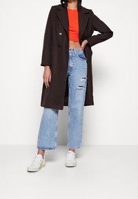 Hnědý dlouhý kabát s dvouřadým zapínáním, kombinovaný s červeným crop topem a světle modrými roztrhanými širokými džíny. Bílé tenisky se žlutým akcentem.