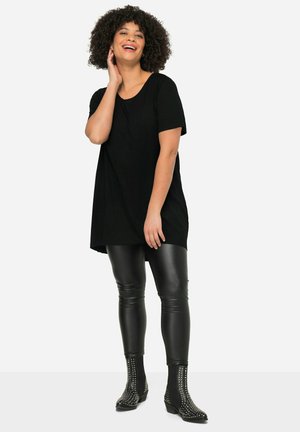 Black oversized t-shirt with short sleeves, paired with shiny black leggings and studded ankle boots. Model displays a relaxed fit.