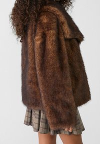 Nepbont bruine jack met een losse fit en een brede kraag. Kenmerkt zich door een zachte textuur en een iets ruige uitstraling. Gestyled met een geruite rok.