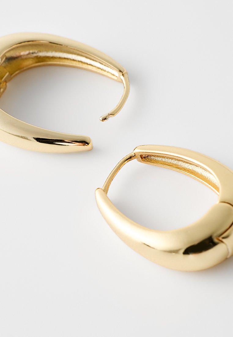 Goldfarbene Hoop-Ohrstecker mit einem runden, klobigen Design. Glatte Oberfläche mit glänzendem Finish. Öffnungen erzeugen einen modernen, minimalistischen Look.
