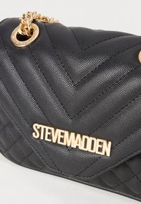Black quilted handbag made of textured material, featuring a gold metal logo, chain detail, and a chevron pattern.