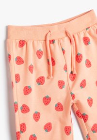 Los pantalones de chándal color durazno presentan un estampado de fresas rojo y verde en toda su superficie, con una cinturilla acanalada y detalle de cordón ajustable.