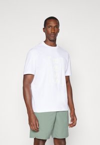 Λευκό κοντομάνικο μπλουζάκι με ανάγλυφο λογότυπο "BOSS", σε συνδυασμό με ανοιχτό πράσινο σορτσάκι, που αναδεικνύει ένα μαλακό ύφασμα και απλό σχέδιο.