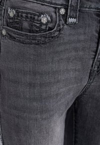 Jeans in denim grigio scuro con cuciture dettagliate sulle tasche e accessori metallici color argento. Visione ravvicinata dell'area delle tasche e della texture.