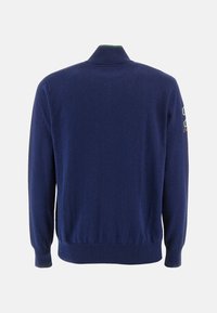 Navy blue knitted sweater with a high collar, ribbed cuffs, and hem. Includes a colorful logo patch on the sleeve. Textured fabric.