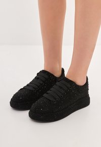 Czarne sneakersy z fakturowaną powierzchnią ozdobioną cyrkoniami, okrągłym noskiem i płaskimi sznurowadłami, zaprojektowane w niskim profilu z amortyzowaną podeszwą.