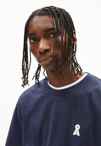 Marineblauwe sweatshirt met ronde hals, voorzien van een wit logo op de linkerkant van de borst en een textuurafwerking.